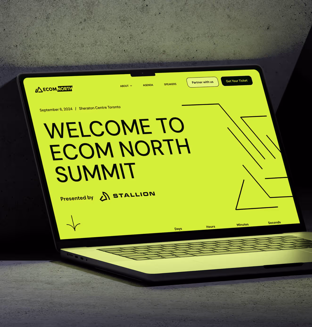A laptop screen displays the Ecom North Summit website with a neon yellow background. The bold black text reads, “Welcome to Ecom North Summit, September 6, 2024, Sheraton Centre Toronto,” presented by Stallion.