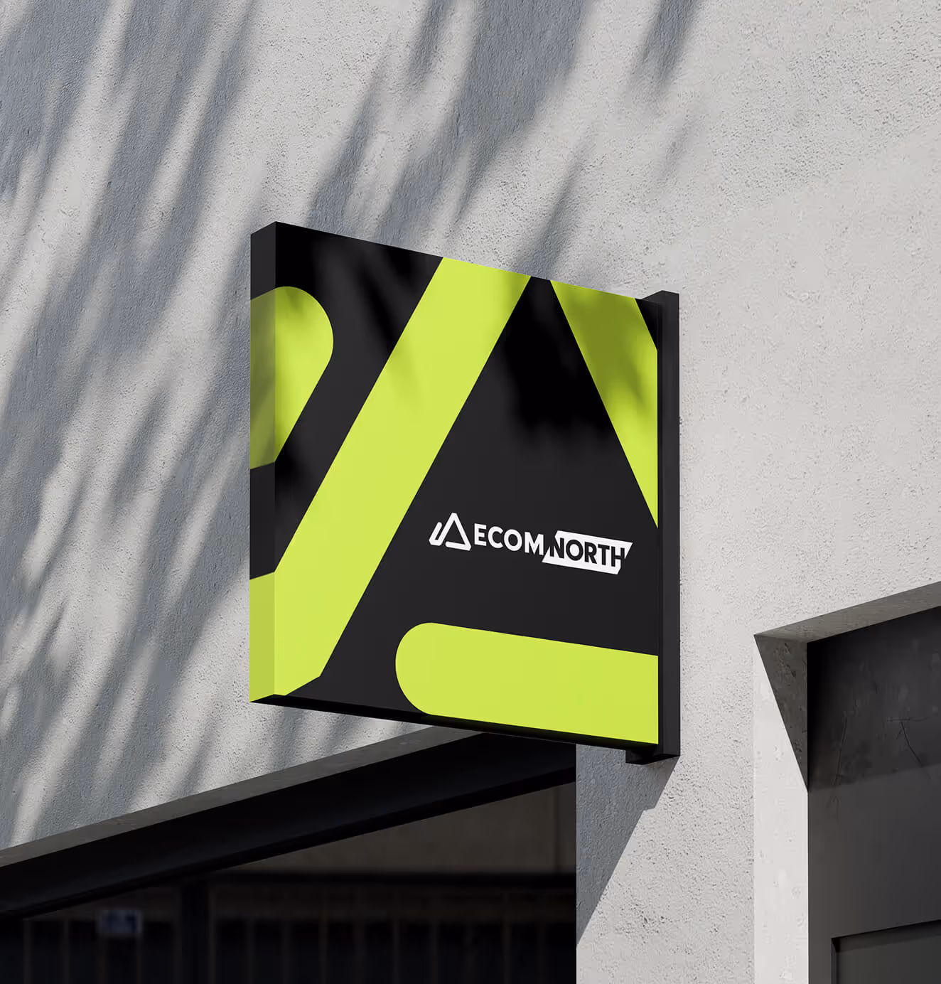 An outdoor wall-mounted sign for Ecom North featuring a large neon green geometric “A” shape on a black background with the event logo in white.