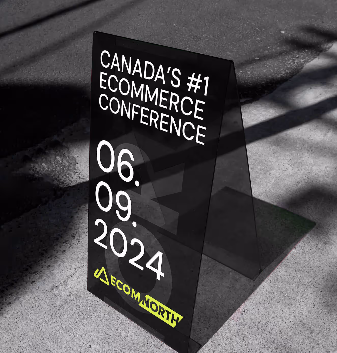 A black sidewalk sign promoting Ecom North Summit with the text “Canada’s #1 eCommerce Conference” and the event date, September 6, 2024. The neon yellow logo is displayed at the bottom.