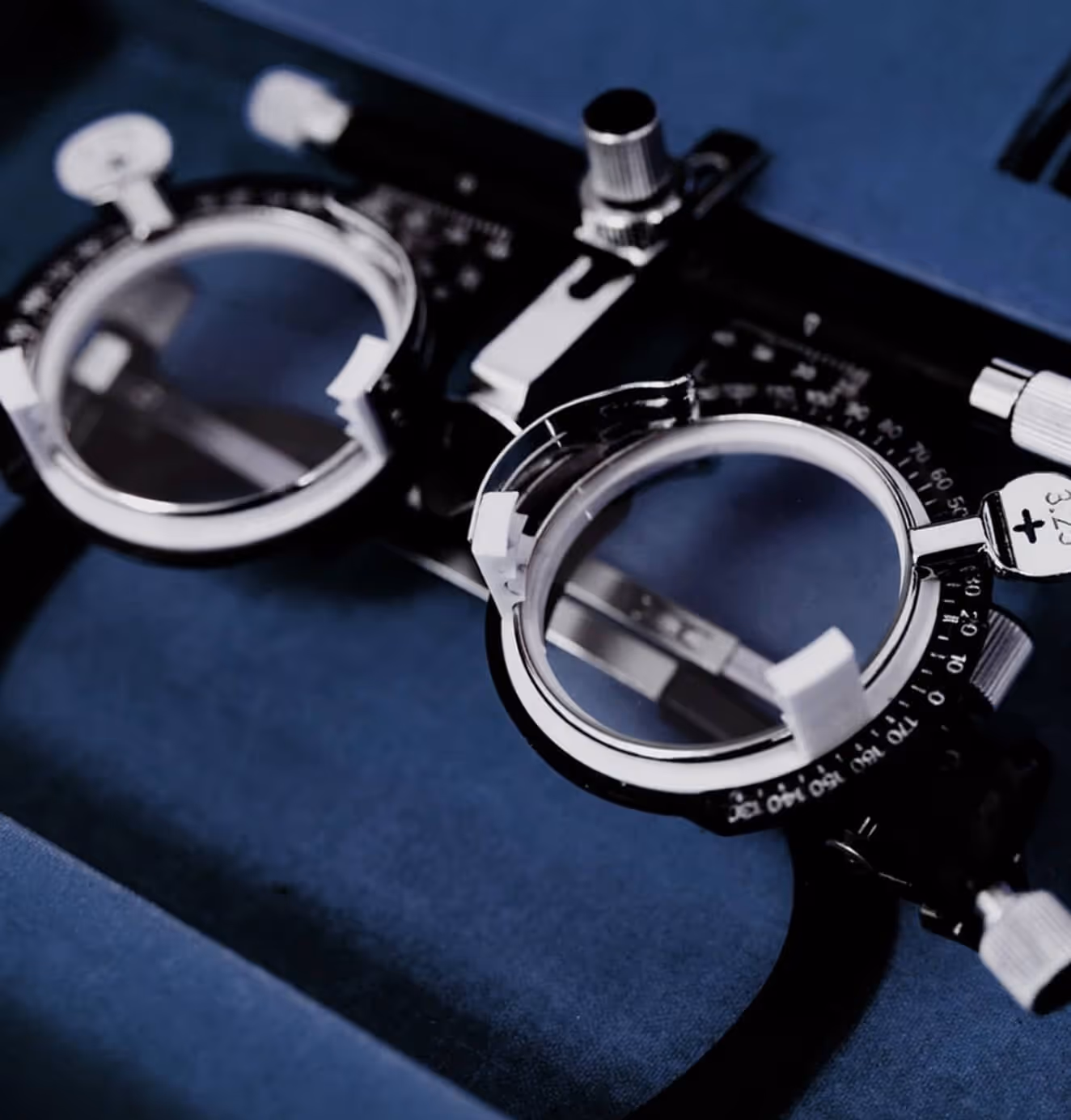 Close-up of a pair of black and silver optometry trial frames placed on a dark blue surface.