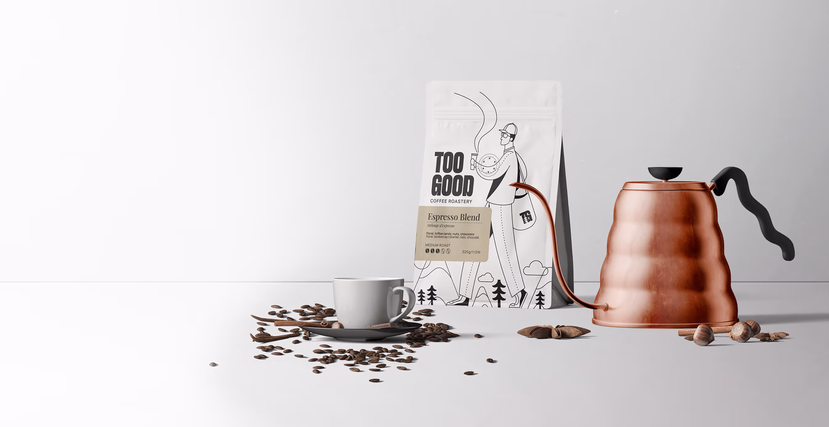A copper gooseneck kettle, white coffee cup, and scattered beans sit beside a Too Good Coffee Roastery bag labeled “Espresso Blend” against a minimalist white background.
