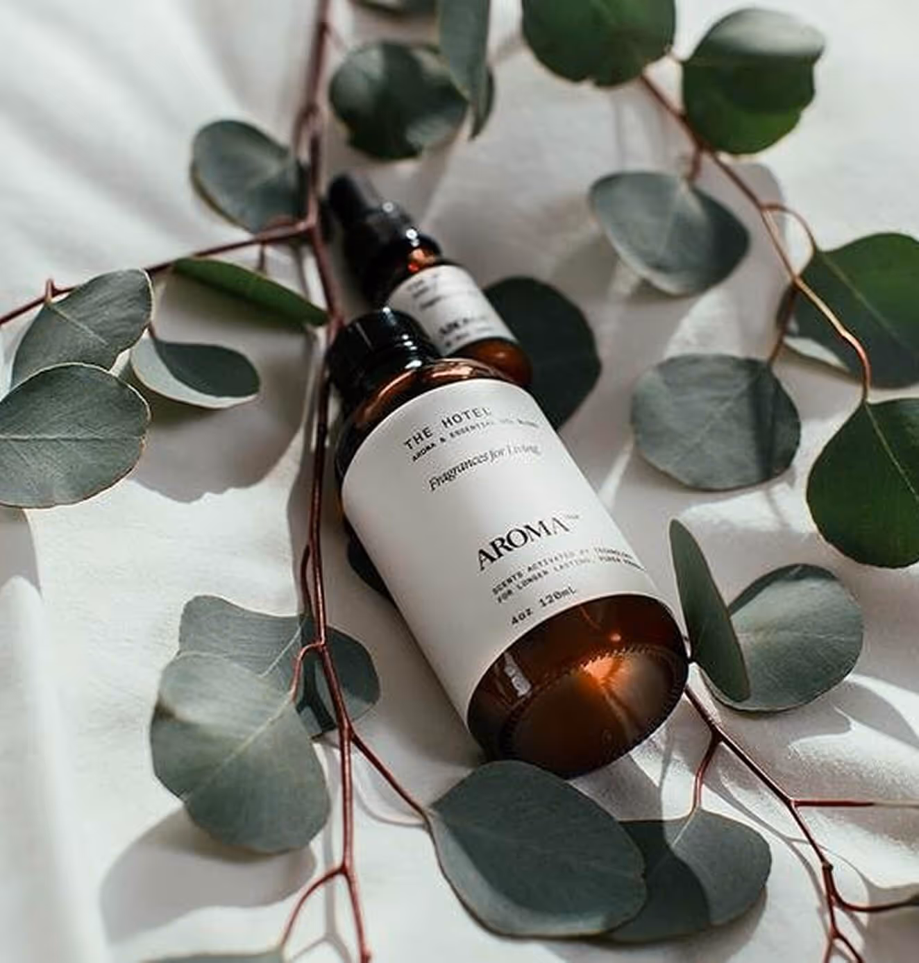 Aromatech essential oil bottles styled on white fabric surrounded by fresh eucalyptus leaves.