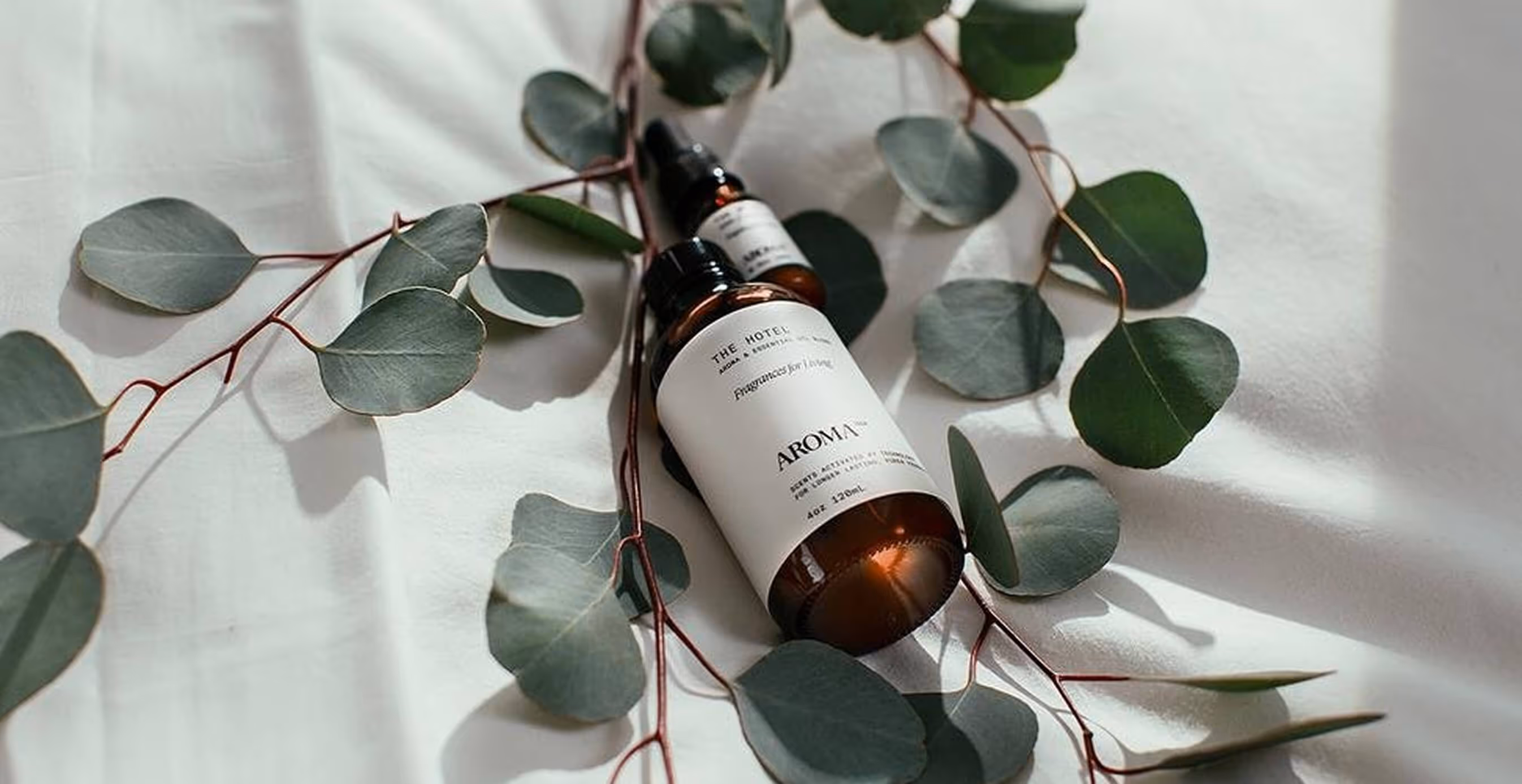 Aromatech essential oil bottles styled on white fabric surrounded by fresh eucalyptus leaves.