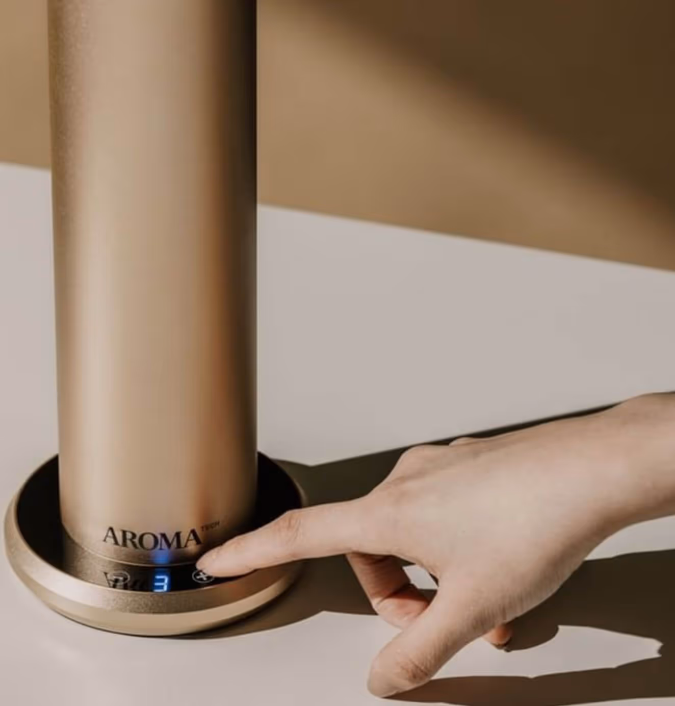 Close-up of a hand adjusting settings on a sleek gold Aromatech diffuser.