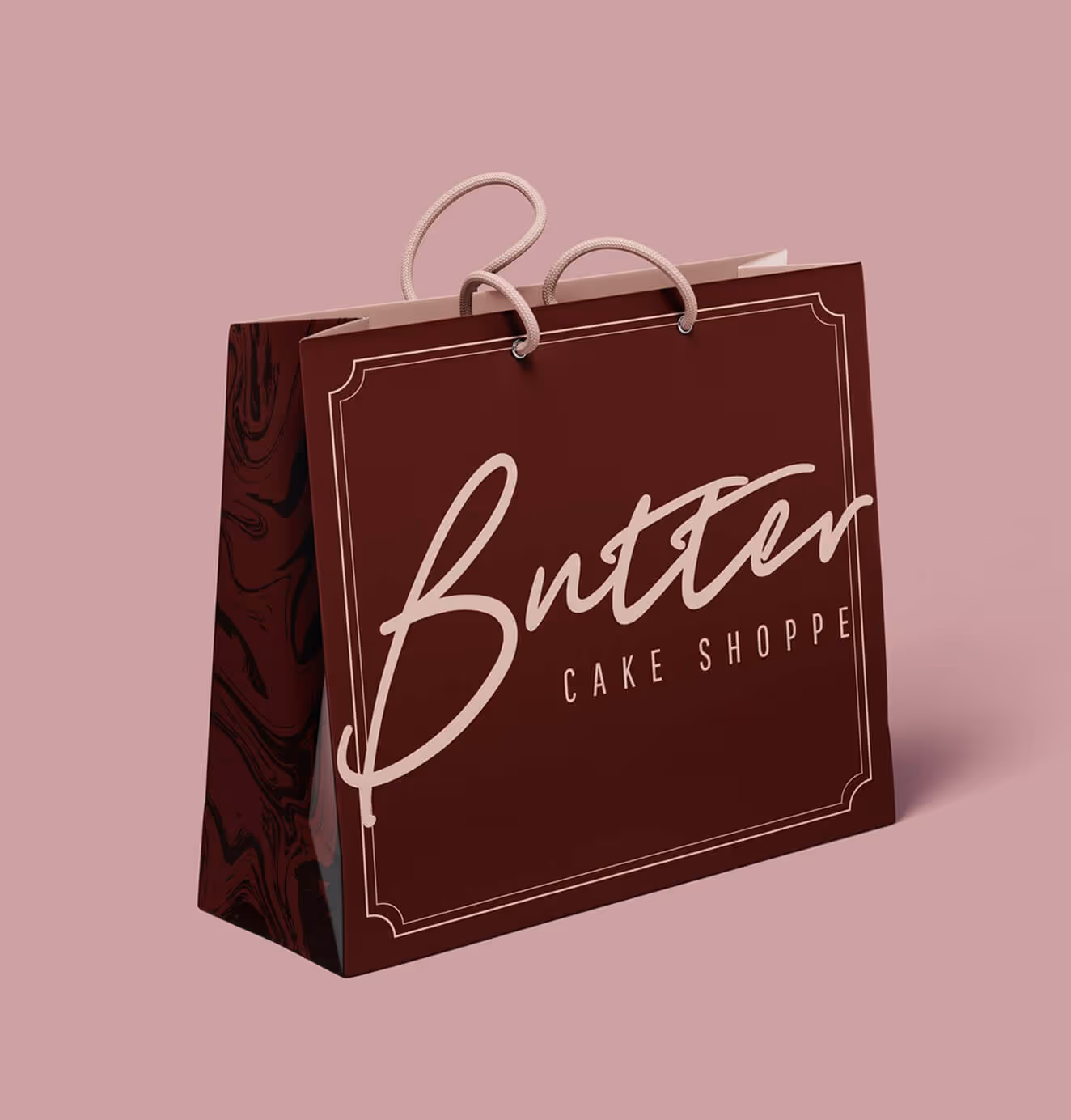 Branded maroon shopping bag with "Butter Cake Shoppe" script logo and decorative frame design against a pink background.