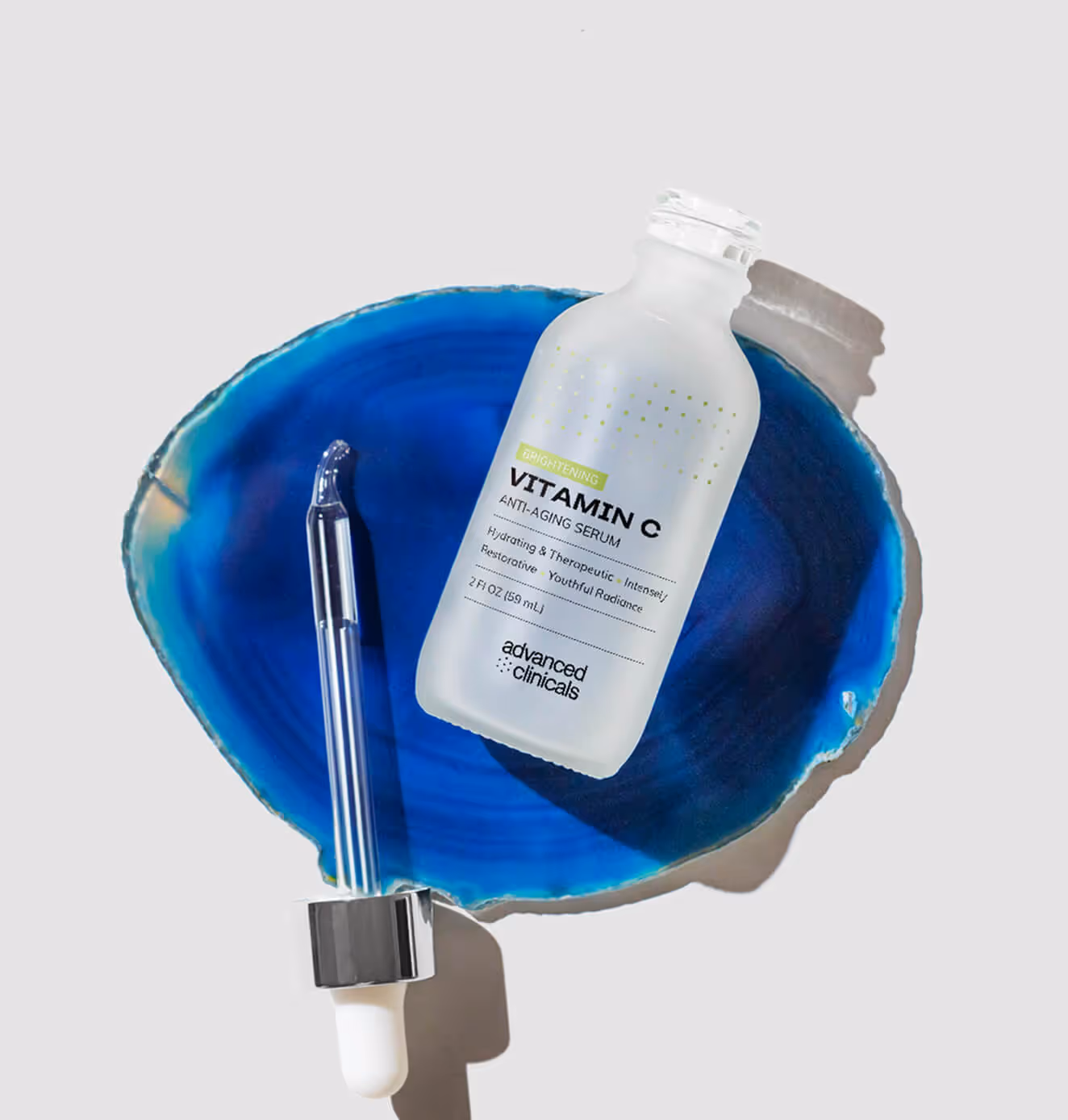 A frosted glass bottle of Advanced Clinicals Vitamin C Anti-Aging Serum with a dropper, styled on a vivid blue agate stone.
