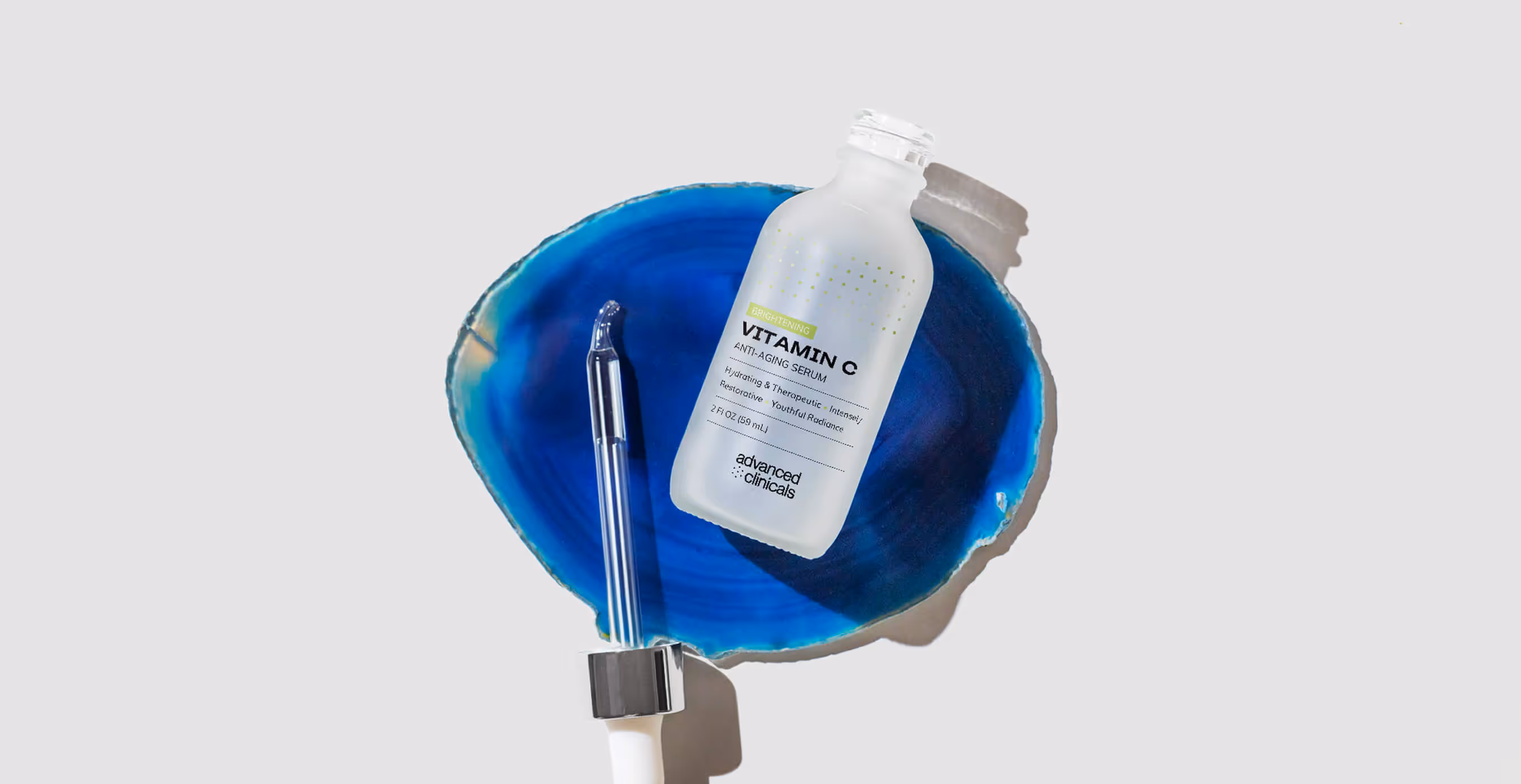A frosted glass bottle of Advanced Clinicals Vitamin C Anti-Aging Serum with a dropper, styled on a vivid blue agate stone.