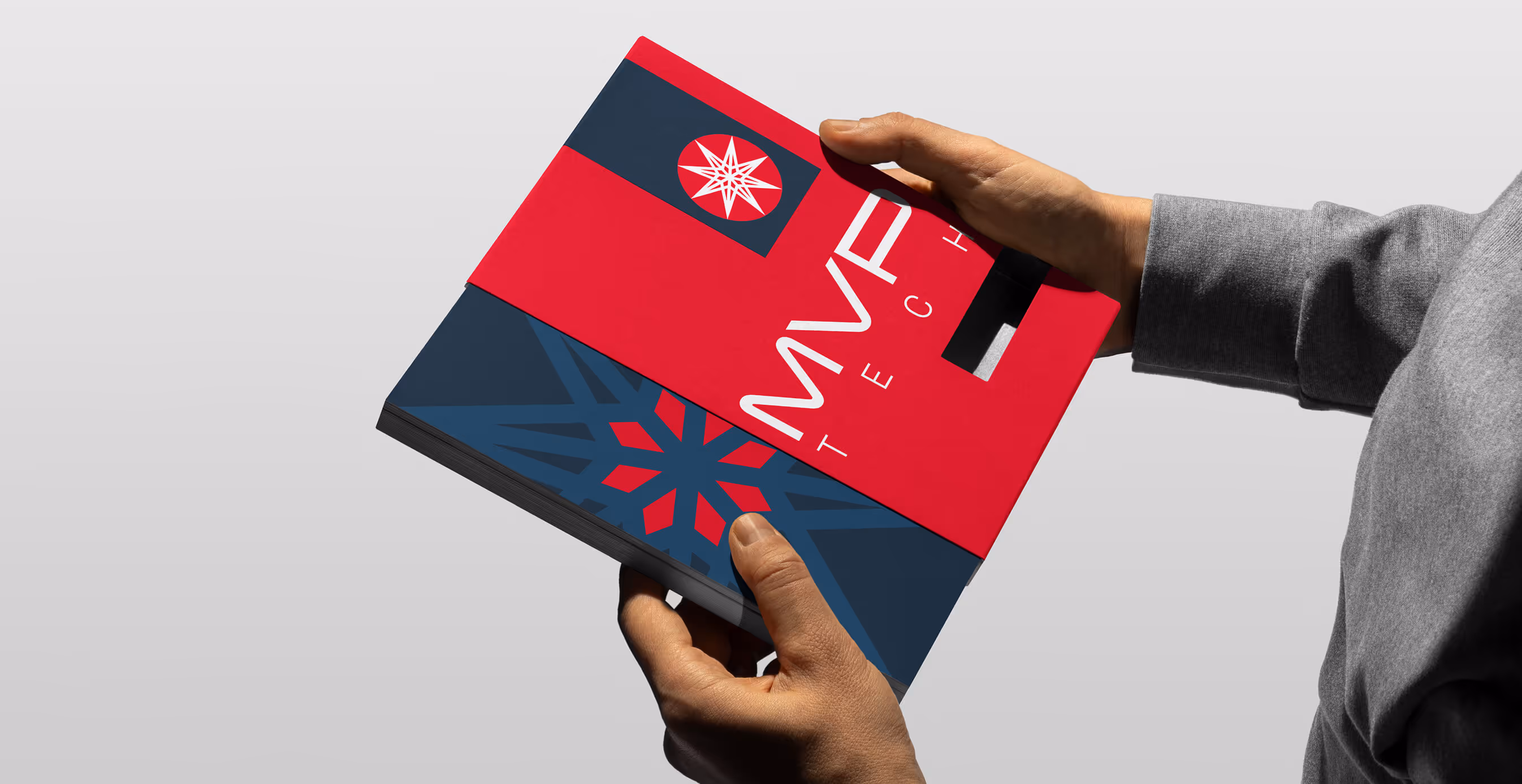Close-up of a person holding a bold red and navy MVP Tech booklet with a geometric compass-like logo, emphasizing modern brand design.