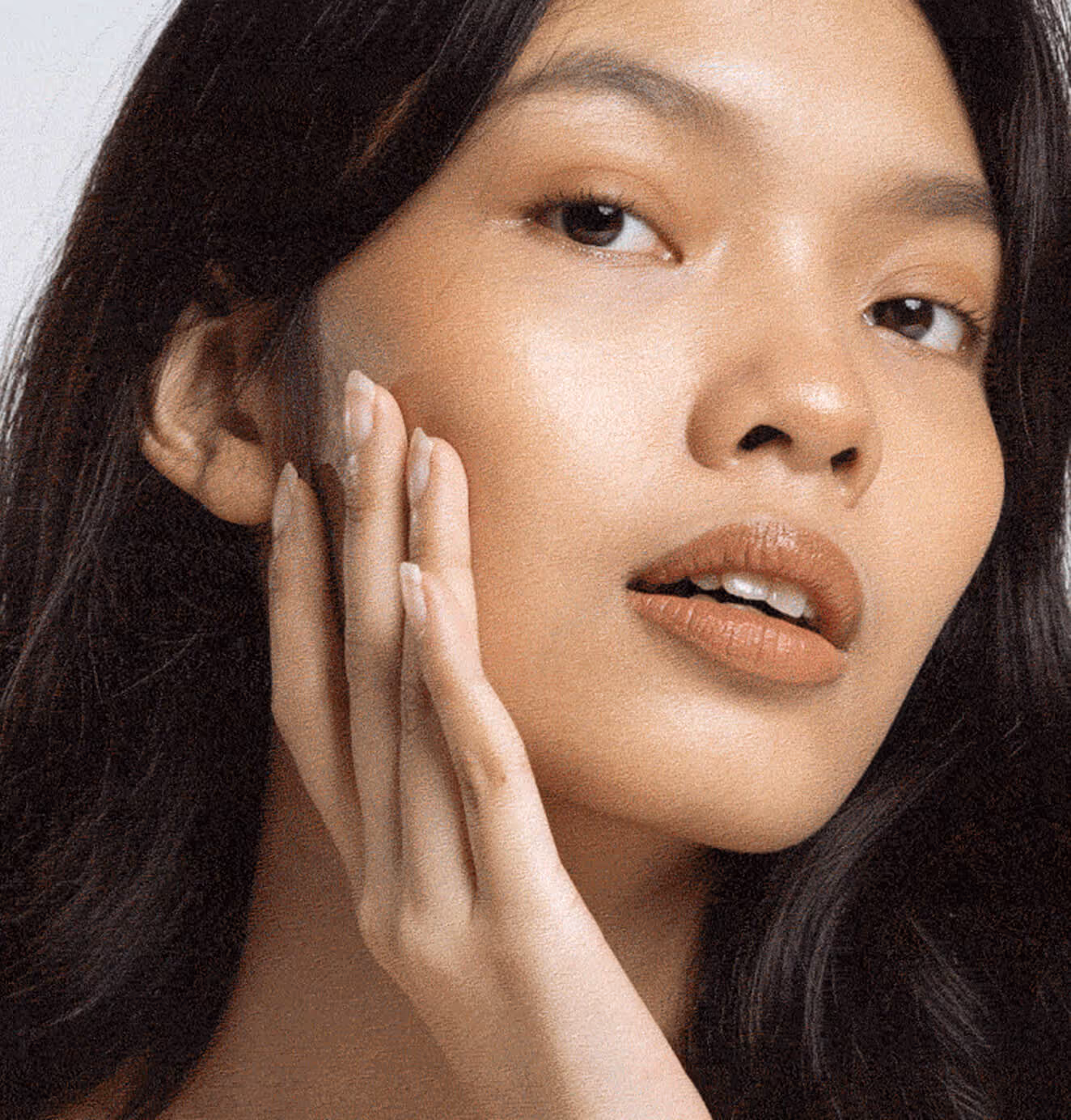 Close-up of a woman with radiant skin touching her cheek, representing the natural, glowing results of Power (Formula) skincare branding.