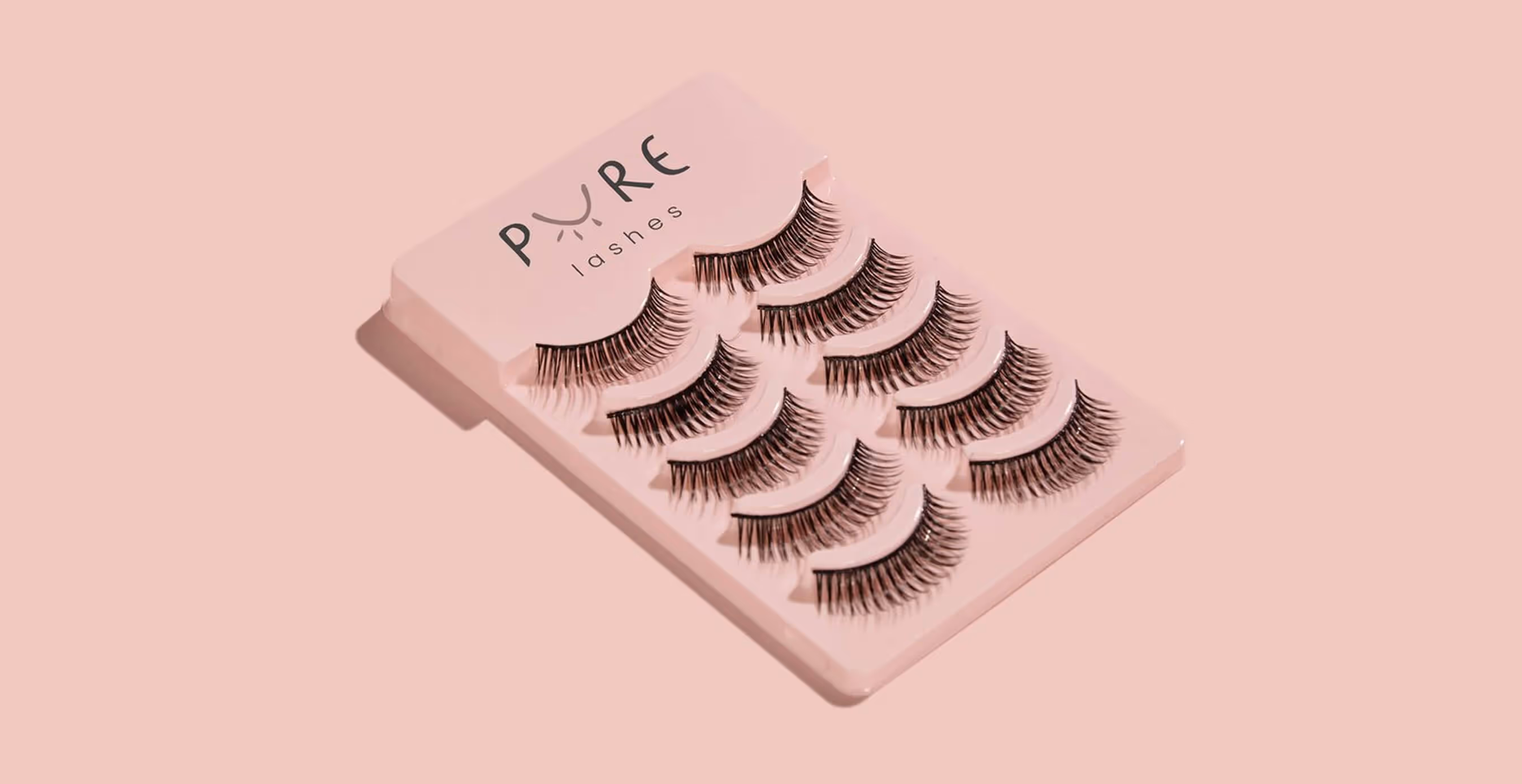 Pink packaging tray displaying multiple pairs of natural fiber Pure Lashes against a blush-toned background.