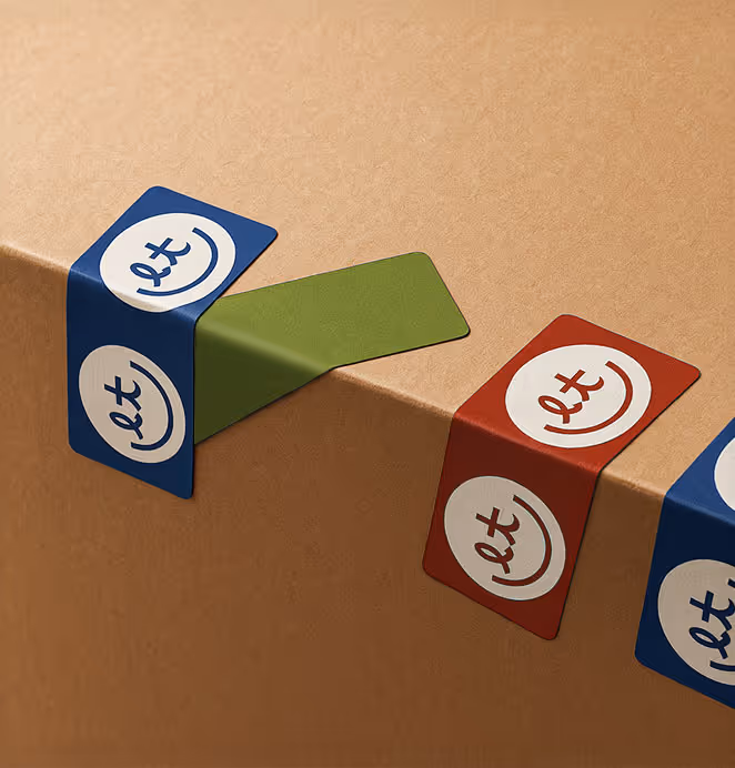 Packaging tape strips in red, blue, and green featuring the Little Tandem circular “lt” logo seal a brown cardboard box.