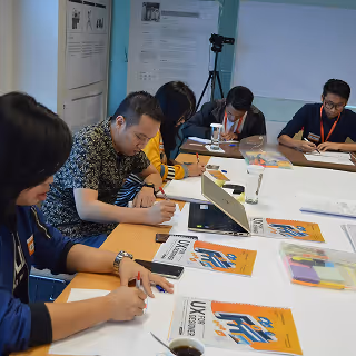 Group of people seated around a conference table taking notes during a UX workshop or training session.