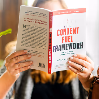 Person holding and reading the book ‘The Content Fuel Framework’ by Melanie Deziel, with a backpack strap visible in the background.