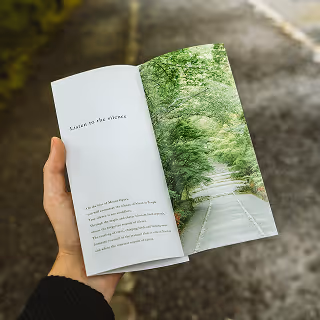Hand holding an open brochure with the phrase “Listen to the silence” and an image of a tree-lined path in nature.