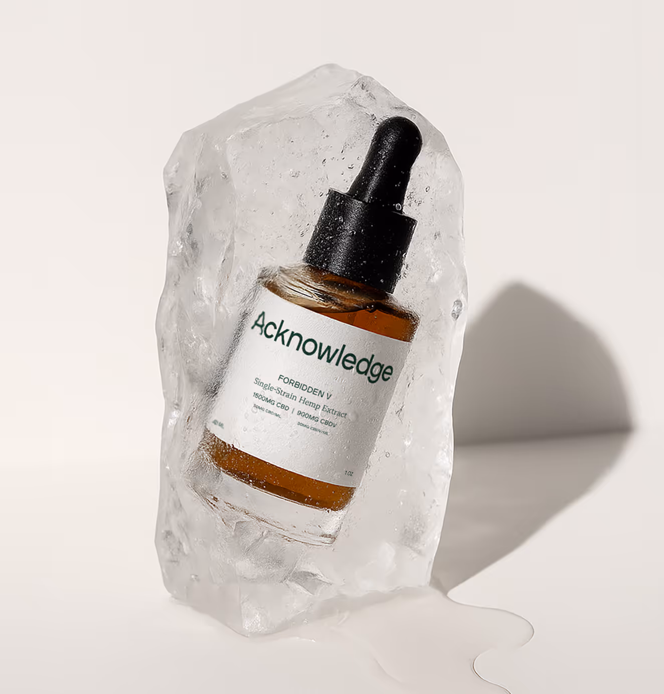 A glass dropper bottle labeled "Acknowledge" is embedded in a partially melted block of ice. The amber liquid inside the bottle contrasts with the clear ice, and the label reads “FORBIDDEN V,” indicating it’s a single-strain hemp extract with CBD and CBG content. The scene is lit with soft shadows on a white background, giving it a clean, minimalist aesthetic.