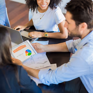 Three team members in a meeting reviewing a tablet displaying colorful charts and graphs, indicating data-driven strategy discussions in marketing.