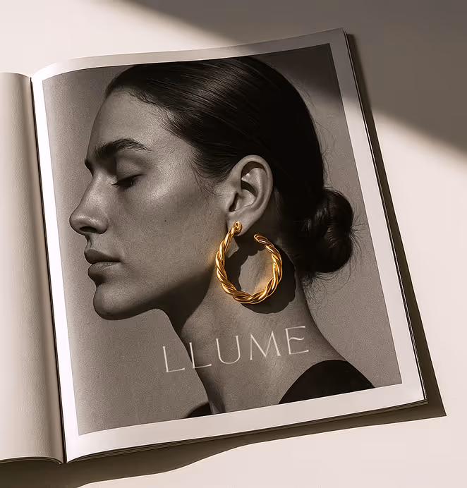 An open magazine featuring a black-and-white portrait of a woman in profile with her hair in a sleek bun, wearing a large twisted gold hoop earring. The word "LLUME" is printed beneath her chin, partially shadowed by soft natural light.
