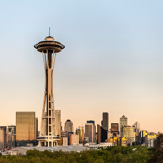 Photograph of the Seattle Space Needle at golden hour, with a clear sky and downtown city buildings bathed in soft evening light.