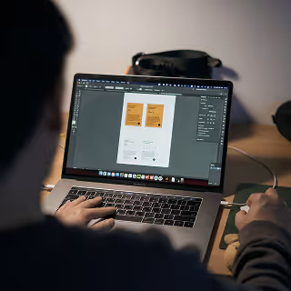 Person working on branding mockups on a laptop screen, showing layout drafts for product packaging or marketing materials.