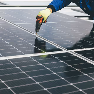 Close-up of a worker using a drill to install solar panels, emphasizing renewable energy and green technology services.