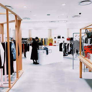 A person shops inside a brightly lit boutique filled with contemporary clothing and accessories, suggesting modern retail presentation and merchandising strategy.