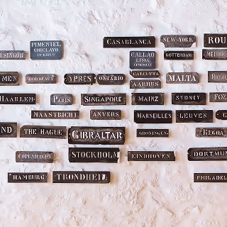 Wall featuring black and white nameplates of cities from around the world, highlighting global inspiration for brand name ideas.