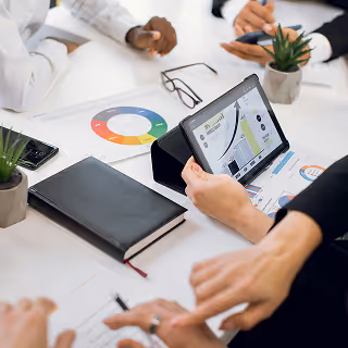Group of professionals sitting at a table analyzing marketing charts and graphs on a tablet and printed materials.