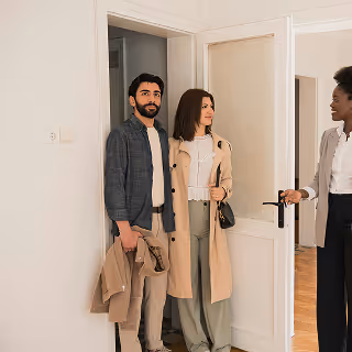 Real estate agent showing a young couple into an apartment, suggesting a property viewing or open house experience.