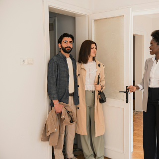 Real estate agent showing a young couple into an apartment, suggesting a property viewing or open house experience.