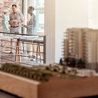Two real estate professionals standing near a scale model of a residential development, discussing property or branding strategies.