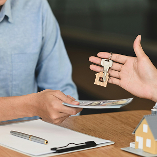 Close-up of one person handing over house keys and documents to another, symbolizing the final stage of a home purchase.