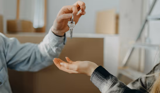 Hand giving keys to another person indoors, representing the trust and relationship between agent and client.