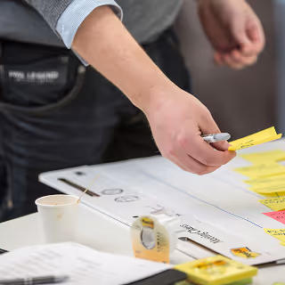A person placing sticky notes on a whiteboard during a branding workshop, surrounded by office supplies and planning tools.