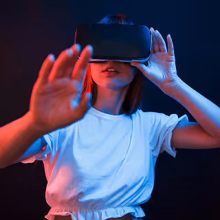 Young woman wearing a VR headset and white t-shirt, reaching forward as if interacting with a virtual environment, showcasing immersive metaverse experiences.