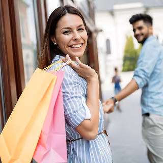 Smiling woman holding colorful shopping bags while walking with a partner, depicting brand loyalty and positive customer experience.