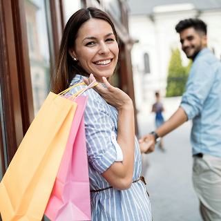 Smiling woman holding colorful shopping bags while walking with a partner, depicting brand loyalty and positive customer experience.