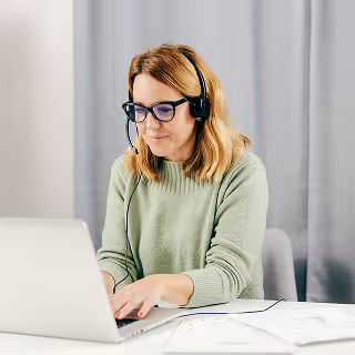 Woman wearing glasses and a headset working on a laptop, representing customer service as a touchpoint in shaping brand perception.