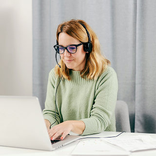 Woman wearing glasses and a headset working on a laptop, representing customer service as a touchpoint in shaping brand perception.