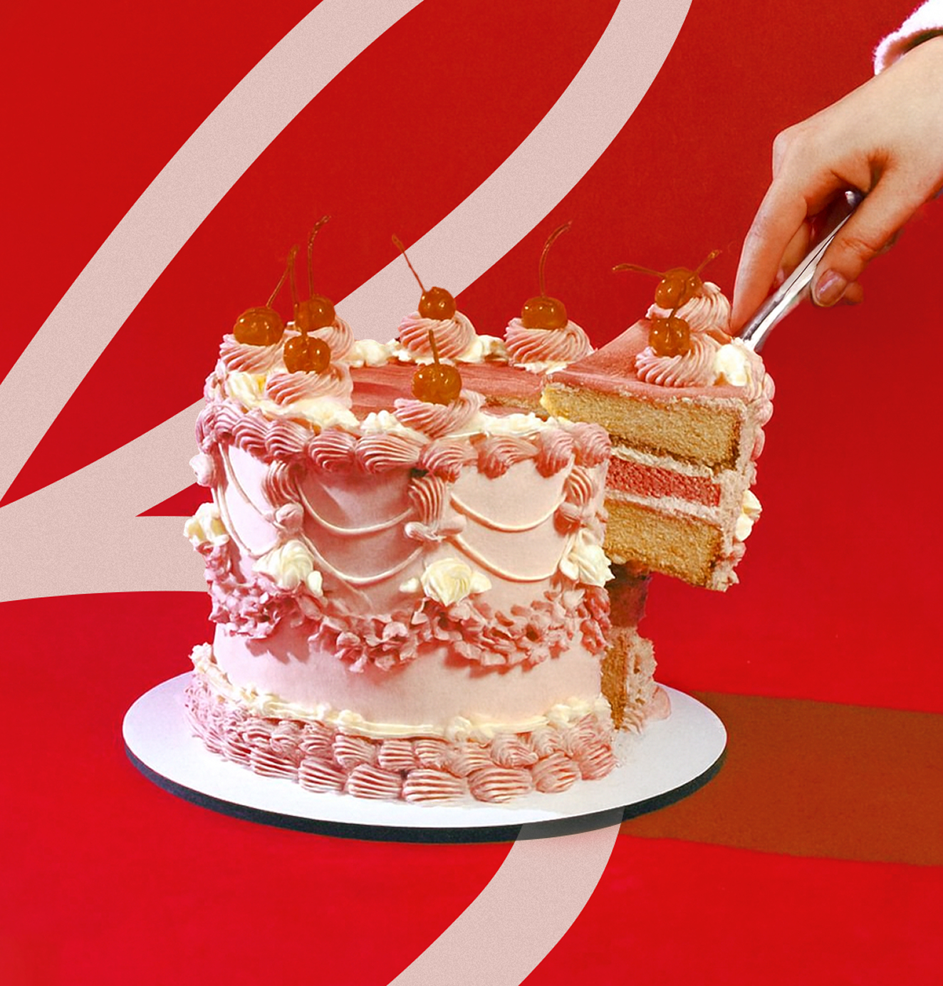Pink frosted layer cake with cherries and piped decorations as a hand lifts out a slice with a cake server.