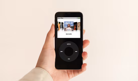 Hand holding a smartphone displaying a music player interface styled like a classic iPod screen, with album art and controls visible.