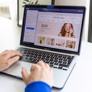 Hands typing on a laptop showing an e-commerce store interface with product images and navigation menus.