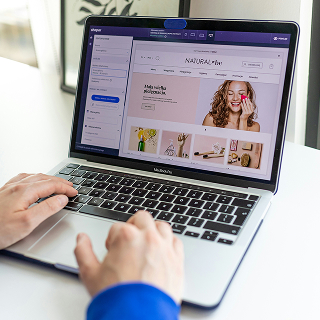 Hands typing on a laptop showing an e-commerce store interface with product images and navigation menus.