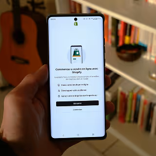 Hand holding a smartphone showing the Shopify app in French, with options to start an online store.