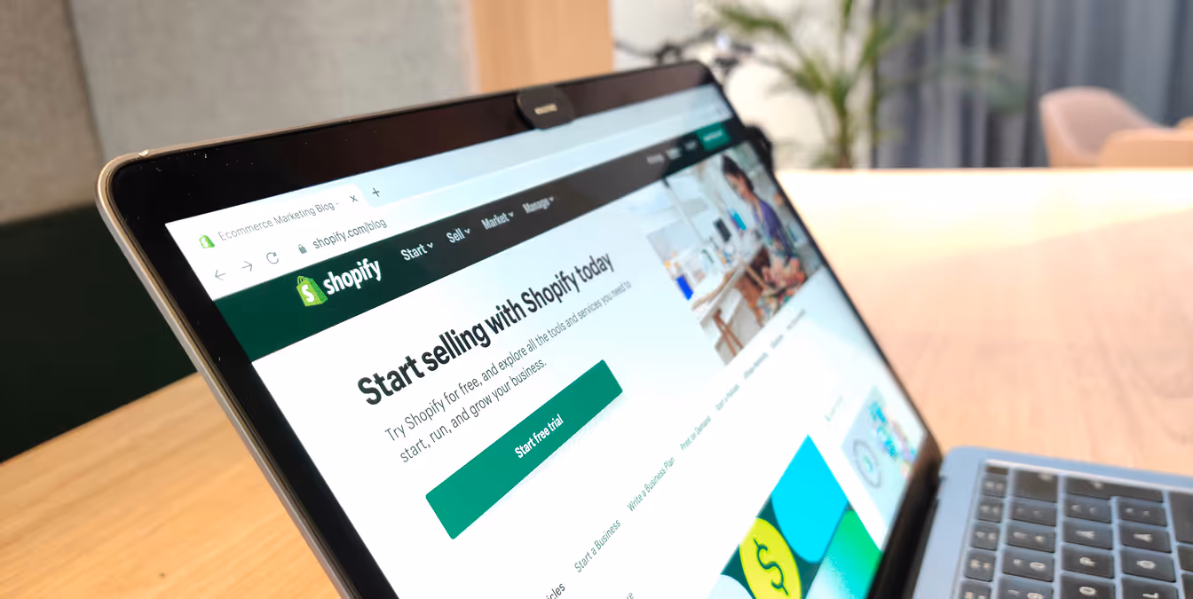 Close-up of a laptop screen displaying the Shopify website with the headline “Start selling with Shopify today” and a green button for a free trial.