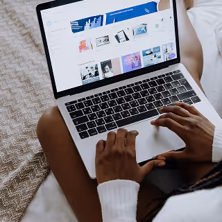 Close-up of a person sitting cross-legged on a bed using a laptop to browse a website with multiple digital templates.