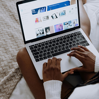 Close-up of a person sitting cross-legged on a bed using a laptop to browse a website with multiple digital templates.