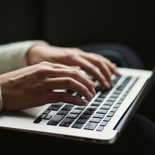 Close-up of hands typing on a laptop keyboard in a dimly lit environment.