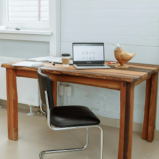 Minimalist workspace with a wooden desk, black chair, coffee cup, papers, and a laptop open to an e-commerce platform.