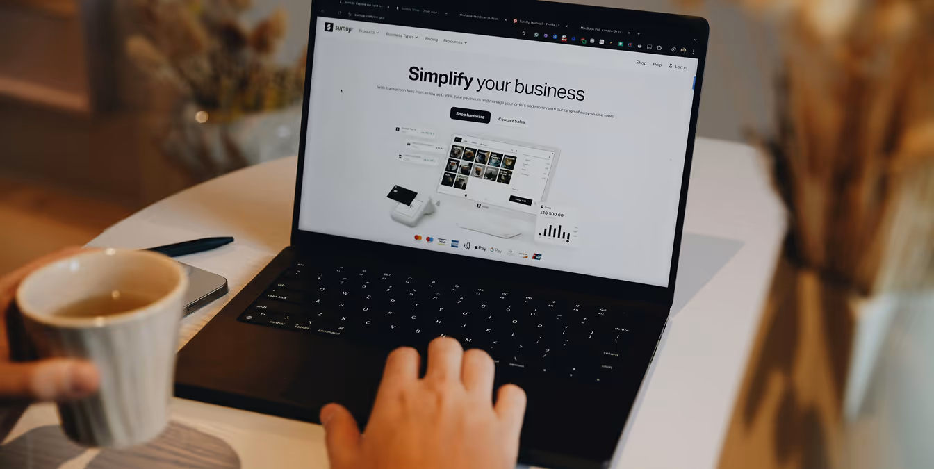 A person holds a coffee cup while using a laptop displaying an e-commerce dashboard with the words "Simplify your business."