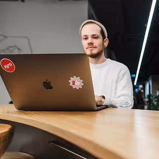 Man in a white sweater working on a laptop at a wooden counter in a modern workspace.
